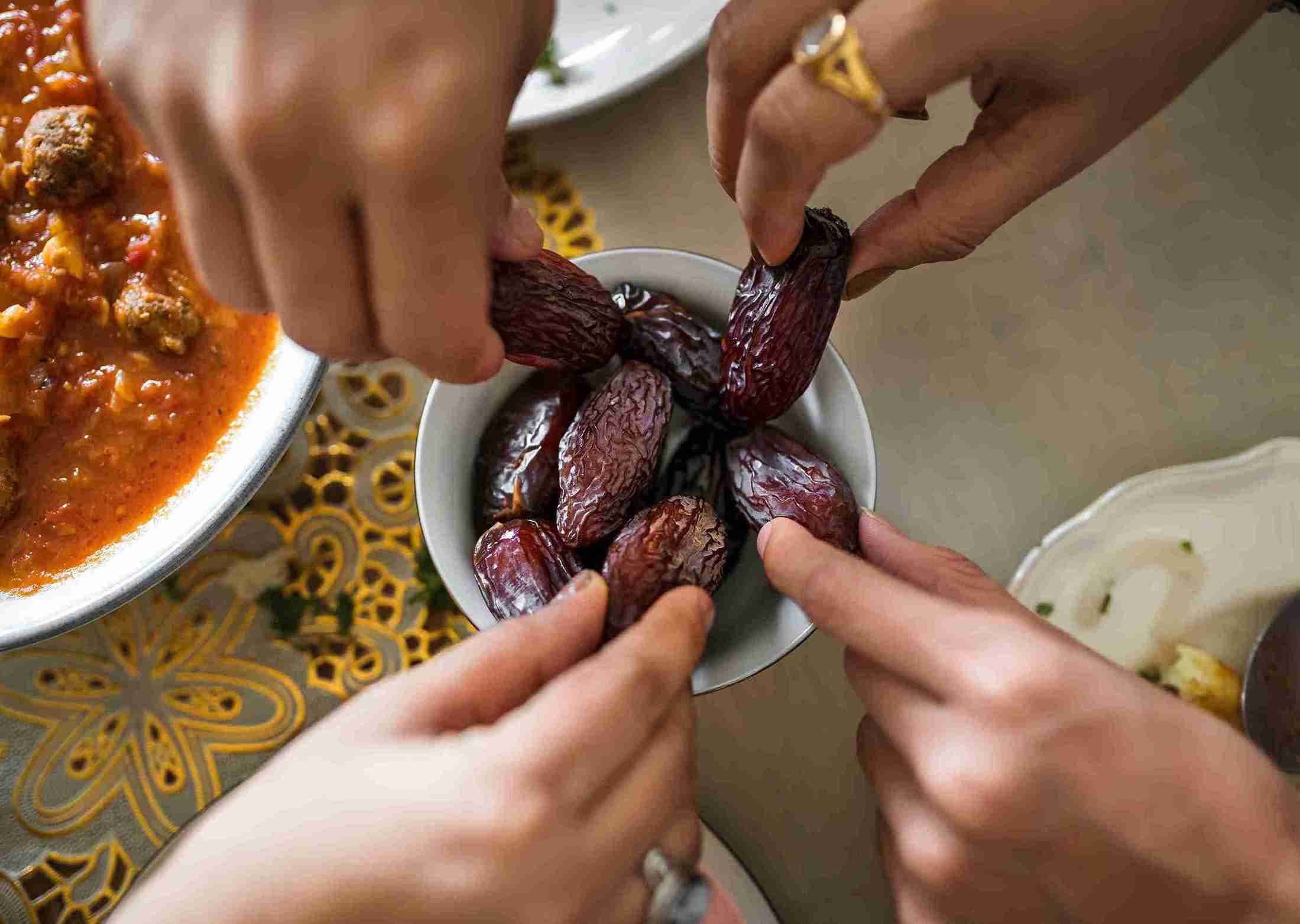 Multiple hands, all reaching for some dates, in an attempt to complete their fast.